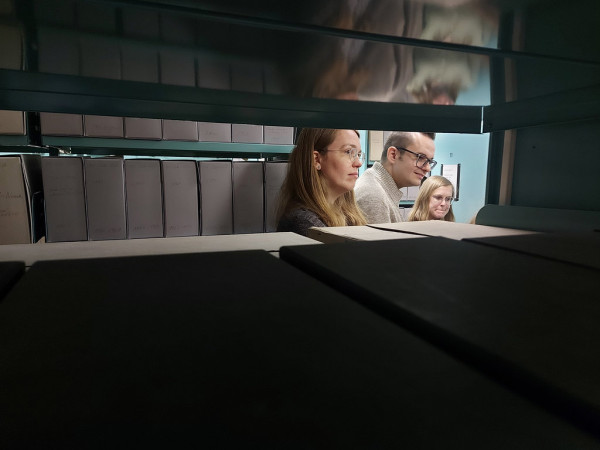 Blick durch Regalanlagen im Nationalarchiv auf Studierende
