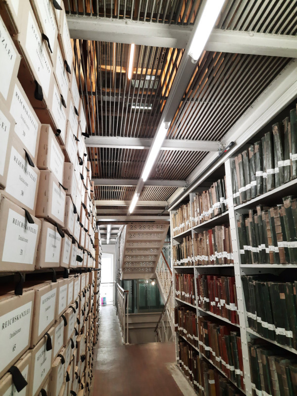 Man sieht durch zwei Regale hindurch auf eine Treppe.