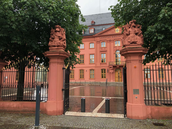 Das Bild zeigt eine Einfahrt, zwei Bäume und dahinter ein rot gestrichenes, prächtiges Gebäude.